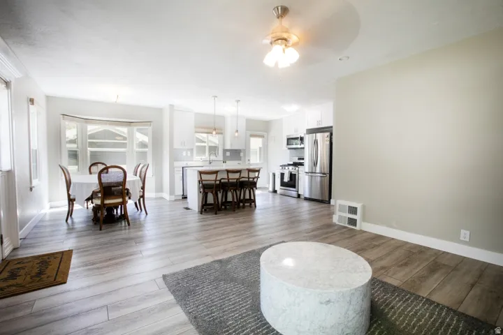 Open-concept living space featuring wood-finish flooring, a bay window, a kitchen island with seating, pendant lighting, and stainless steel appliances