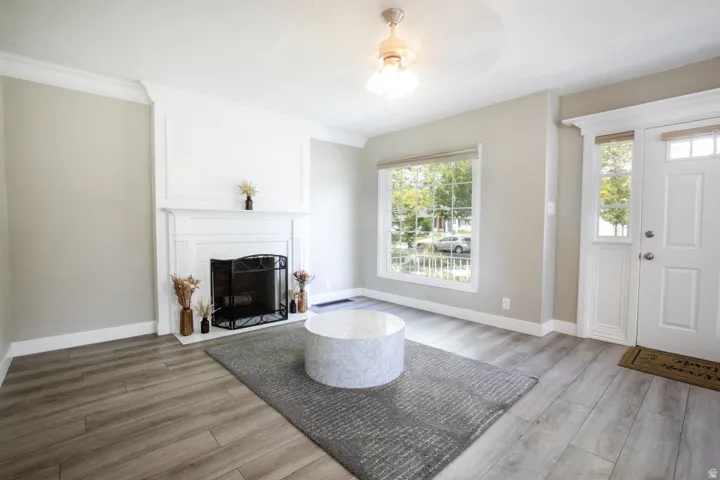 Wood-finish flooring throughout, white fireplace with decorative mantel, crown molding, and a front entry door with transom window