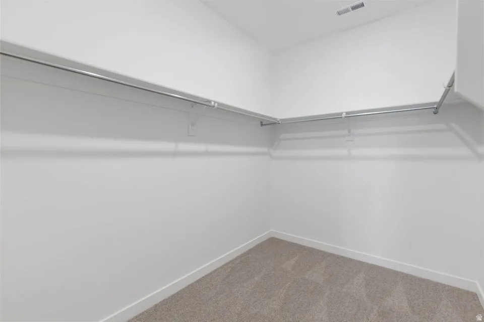 Expansive walk-in closet with clean white walls and durable carpet flooring