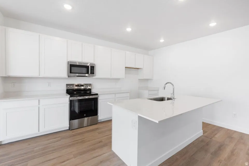 Kitchen featuring white cabinetry, light-toned countertops, stainless steel appliances, and wood-finish flooring