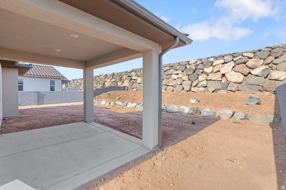 Covered concrete patio with recessed lighting and a stone retaining wall