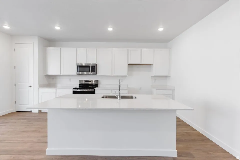 Kitchen featuring an integrated island, white cabinetry, stainless steel appliances, wood-finish flooring, and recessed lighting