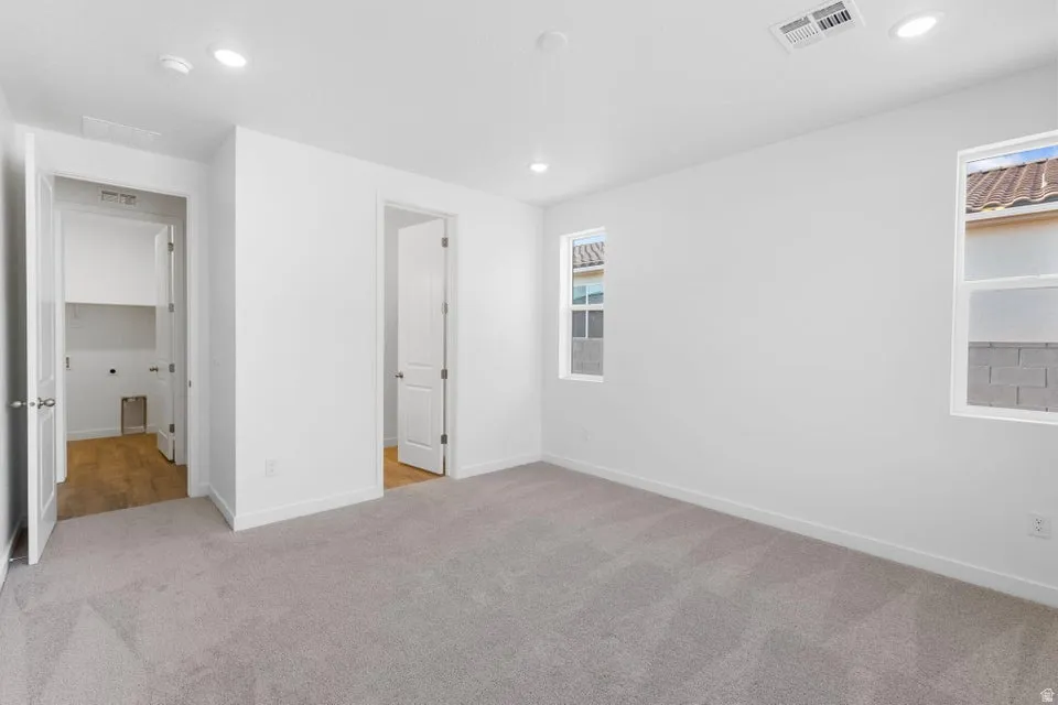 Recessed lighting, light gray carpeting, two windows, two paneled doors, and a laundry area with wood-finish flooring and built-in shelving