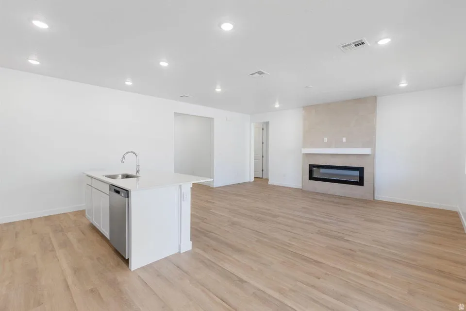 Spacious open-concept interior featuring light wood-finish flooring, recessed lighting, and a contemporary fireplace with a stone-finish surround and white mantel