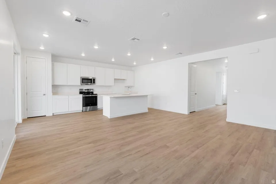 Open-concept living area featuring wood-finish flooring, recessed lighting, a kitchen island, white cabinetry, and stainless steel appliances