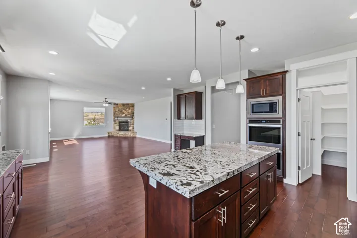 Kitchen island with a granite countertop, built-in stainless steel appliances, and dark wood cabinetry