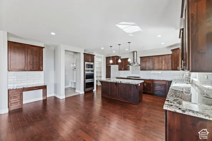 Spacious kitchen featuring wood-finish flooring, dark wood cabinetry, light-toned countertops, a central island, and stainless steel appliances