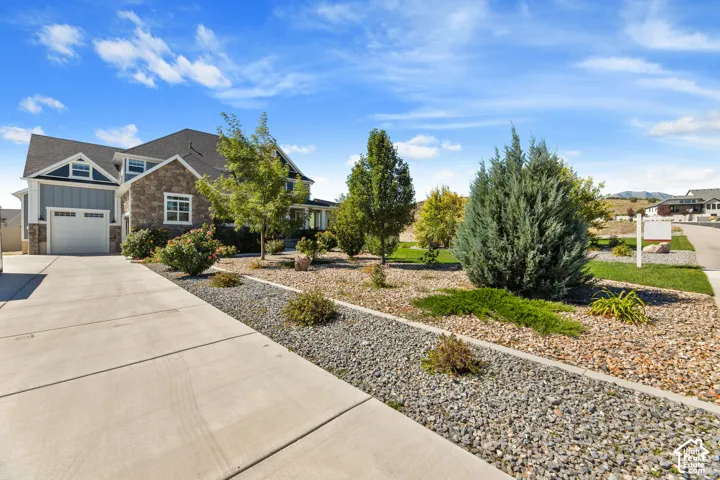 Two-story residence featuring a stone and siding facade, an attached garage, a concrete driveway, and established landscaping with various trees and shrubs