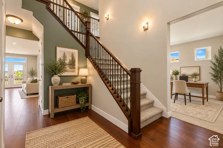 Foyer featuring wood-finish flooring, staircase with a dark wood handrail and decorative metal balusters, and wall-mounted light fixtures