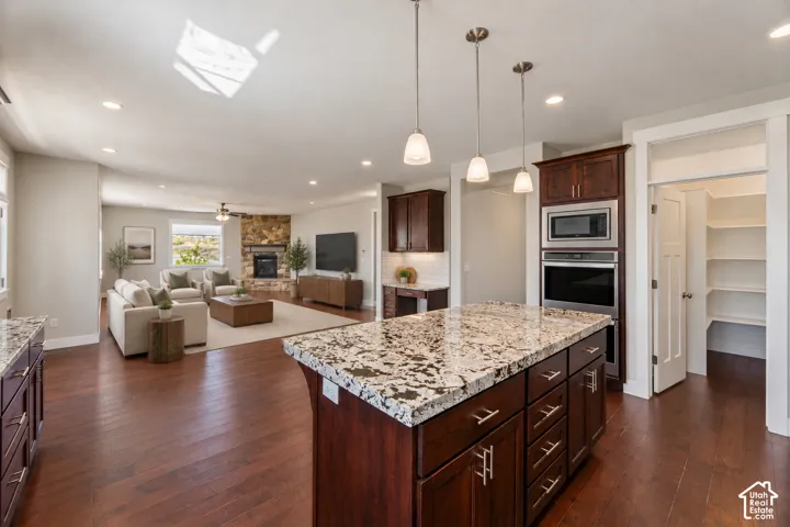 Kitchen featuring a center island with a stone countertop, dark wood cabinetry, recessed lighting, stone-surround fireplace, and wood-finish flooring