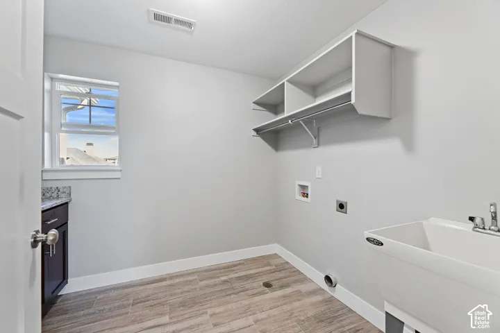 White utility sink, wood-finish flooring, built-in shelving, white cabinetry with a light-toned countertop, and a window providing natural light