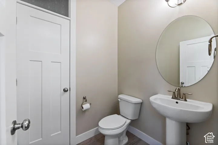 Pedestal sink with brushed nickel faucet, oval mirror, white toilet, and wood-finish flooring