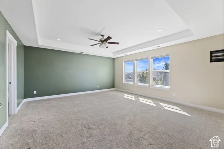 Spacious room featuring a tray ceiling with recessed lighting, ceiling fan, and carpeted flooring