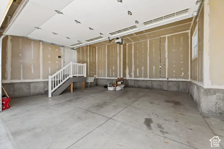 Spacious garage featuring a concrete floor, interior staircase with white railing, and a window for natural light