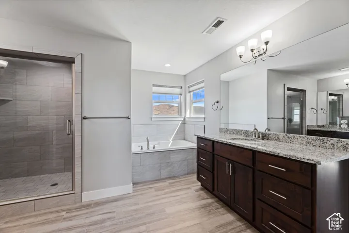 Dual vanity with a speckled countertop, a built-in soaking tub, a tiled shower enclosure, wood-finish flooring, and a multi-bulb light fixture