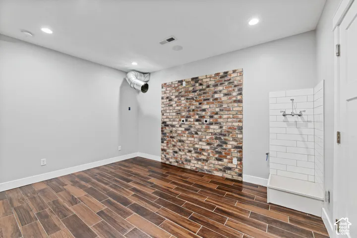 Wood-finish flooring, accent brick wall, recessed ceiling lighting, and a tiled utility sink with wall-mounted plumbing