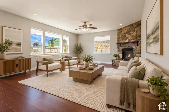 Living area featuring wood-finish flooring, vaulted ceilings, natural stone fireplace surround, dark wood mantel, and large picture windows