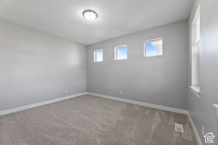 Neutral gray wall paint, plush carpeting, three square windows, one tall vertical window, and a flush-mount ceiling light fixture