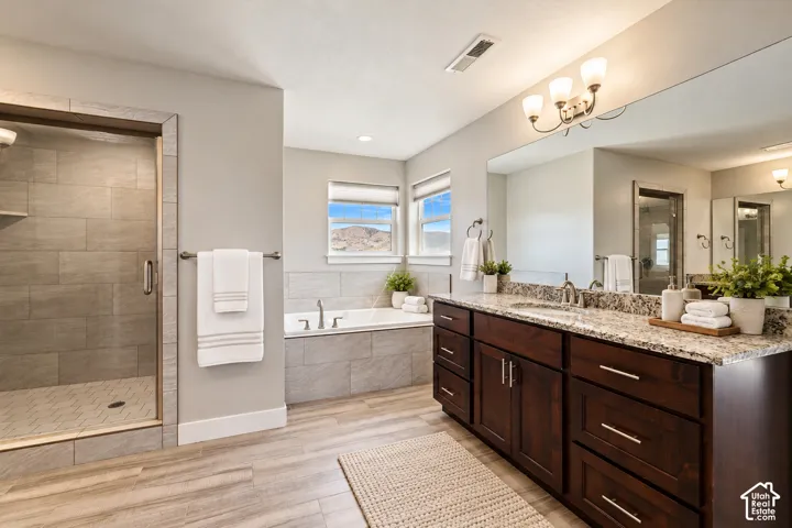 Bathroom featuring a dark wood cabinetry vanity with stone countertop, large wall-mounted mirror, walk-in shower with tiled surround, and a soaking tub with matching tiled finish