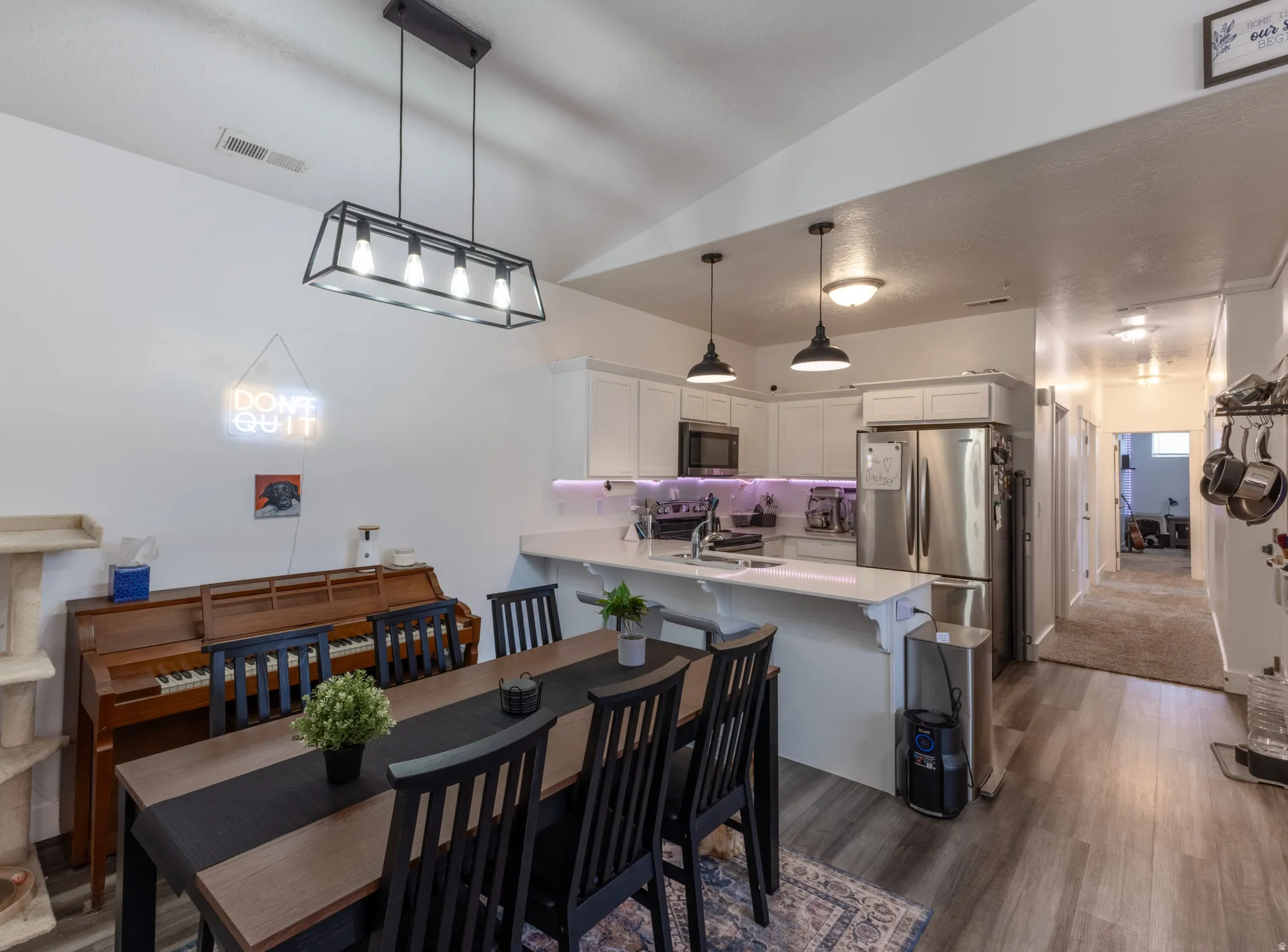 Open-concept living space with vaulted ceilings, wood-finish flooring, and a contemporary linear chandelier