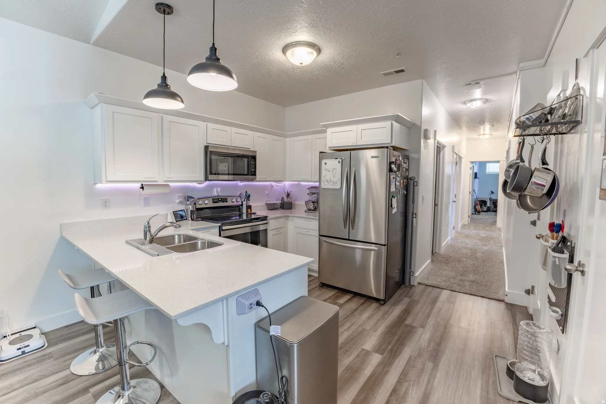 Kitchen featuring white cabinetry, stainless steel appliances, a double basin sink, pendant lighting, and wood-finish flooring