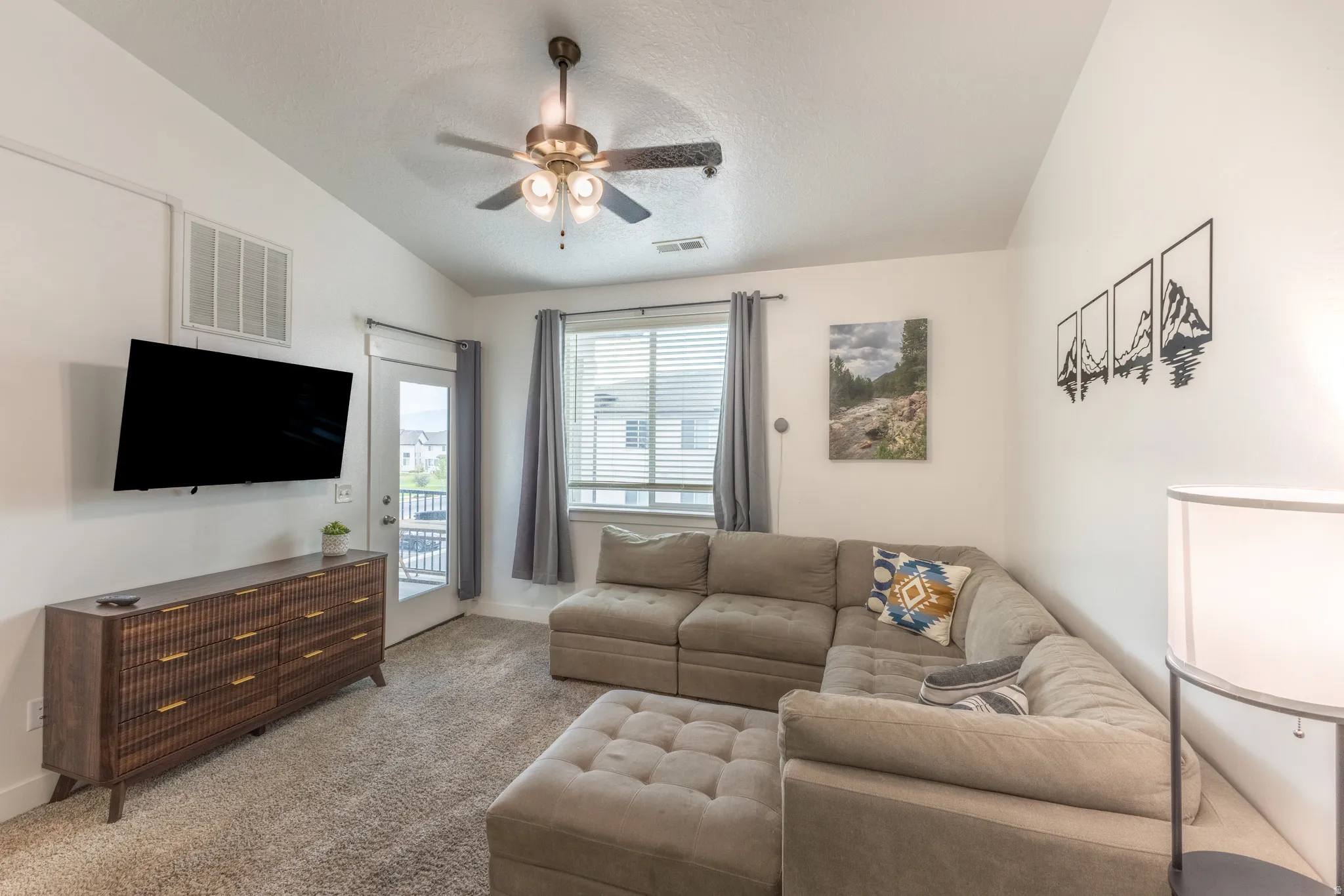 Vaulted ceiling featuring a ceiling fan, light-toned carpeting, and a glass-paneled exterior door