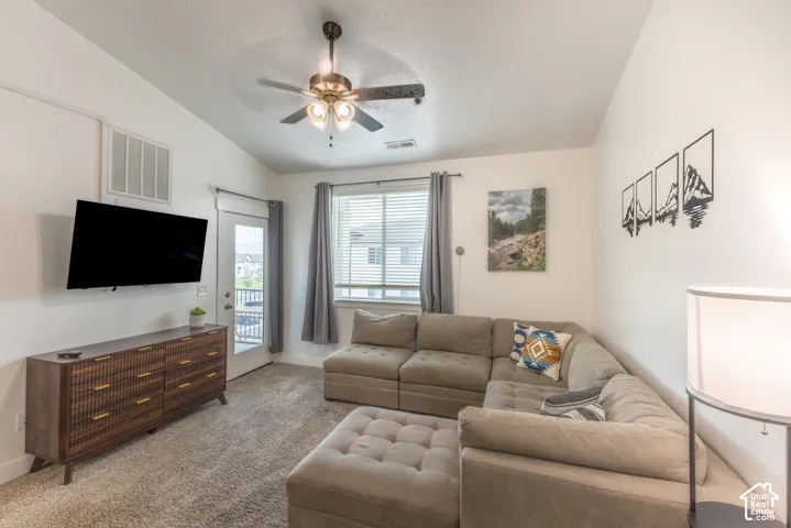 Vaulted ceiling featuring a ceiling fan, light-toned carpeting, and a glass-paneled exterior door