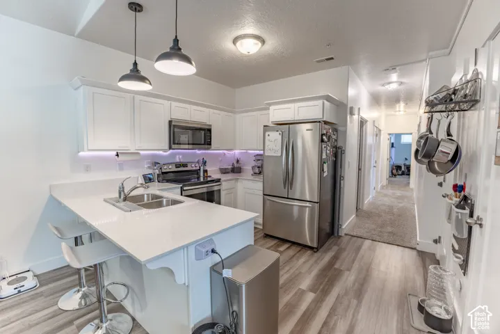 Kitchen featuring white cabinetry, stainless steel appliances, a double basin sink, pendant lighting, and wood-finish flooring