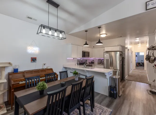 Open-concept living space with vaulted ceilings, wood-finish flooring, and a contemporary linear chandelier