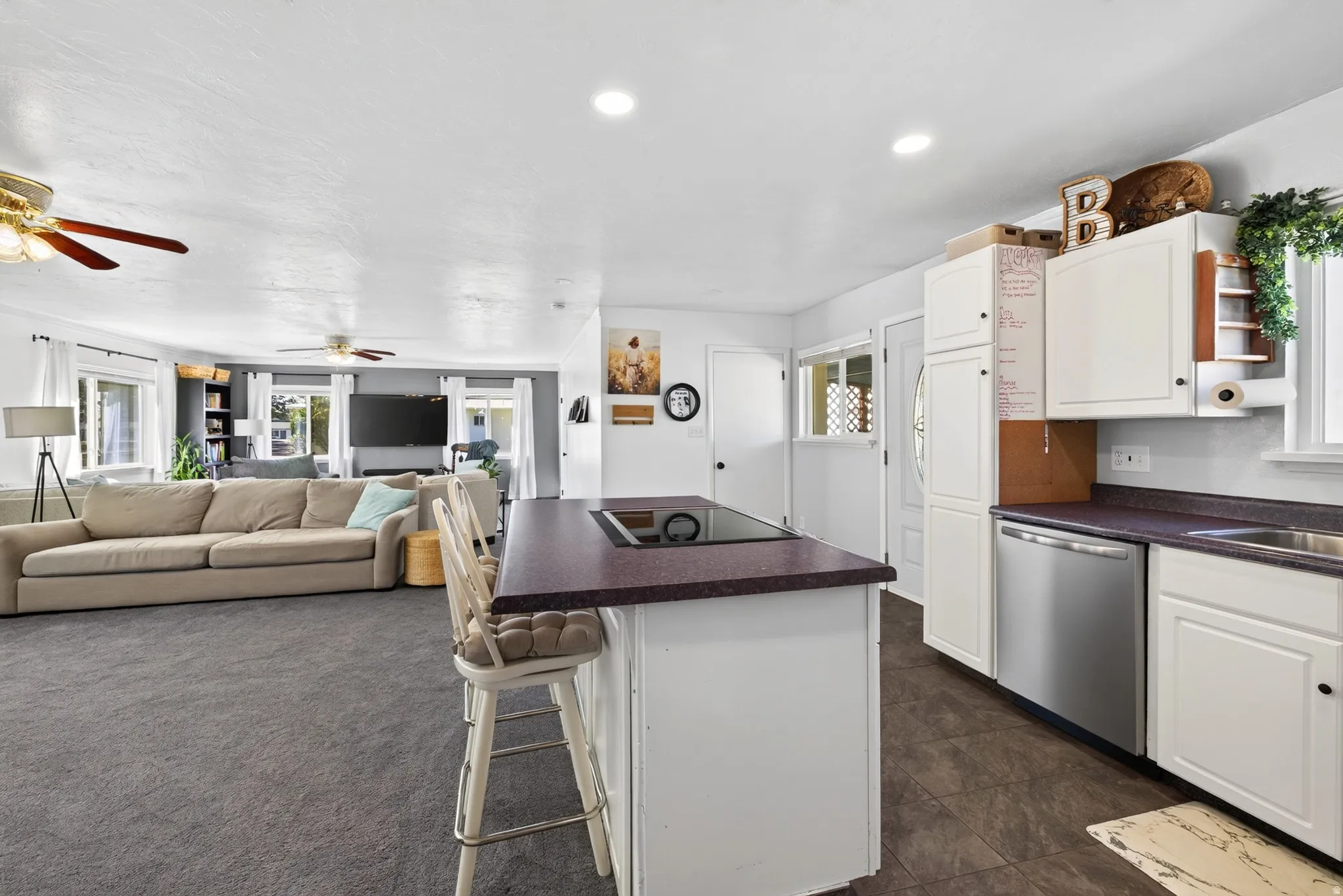 Kitchen island with cooktop and seating, white cabinetry, stainless steel dishwasher, and wood-finish flooring