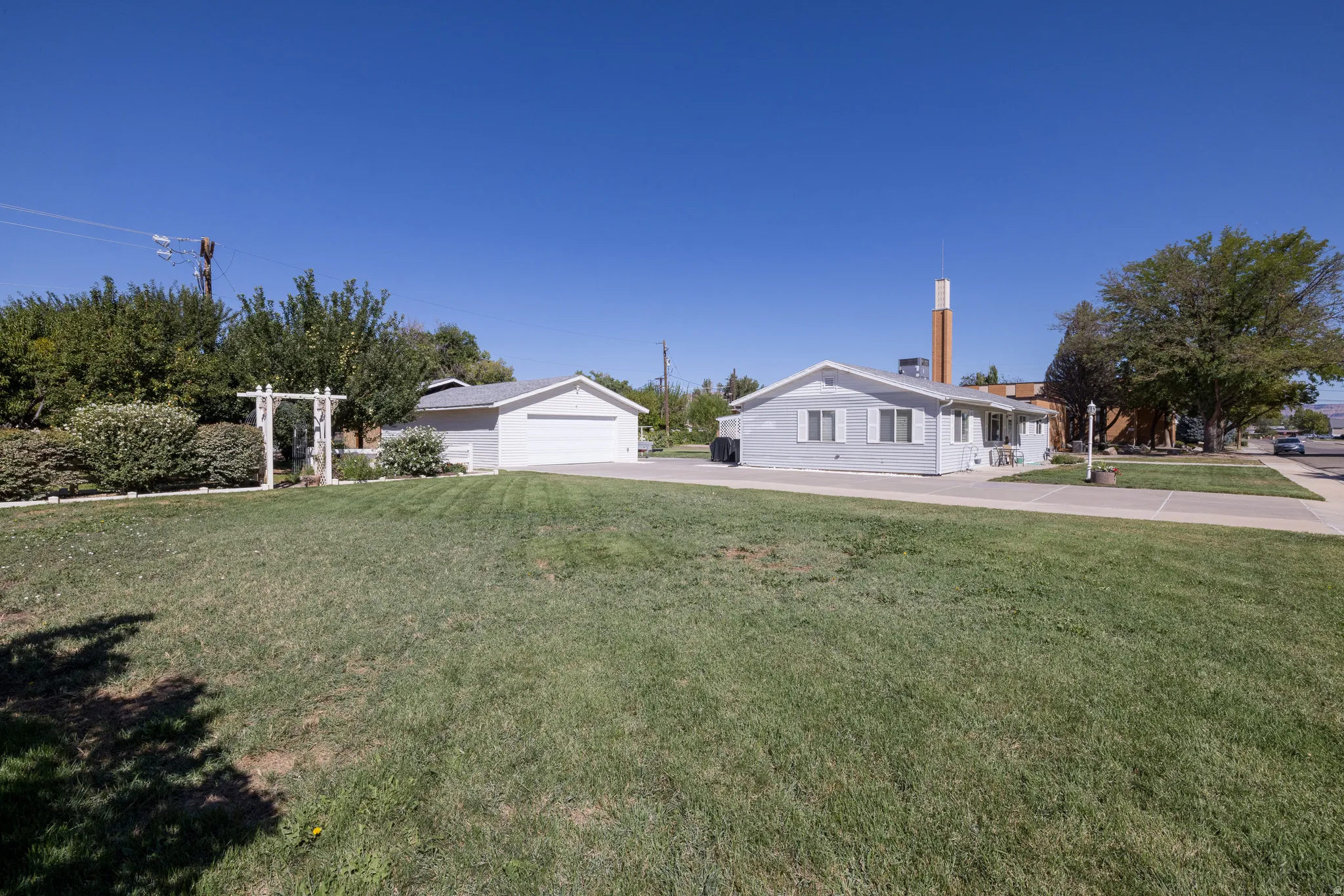 Expansive front lawn with a detached garage and a light-colored exterior residence