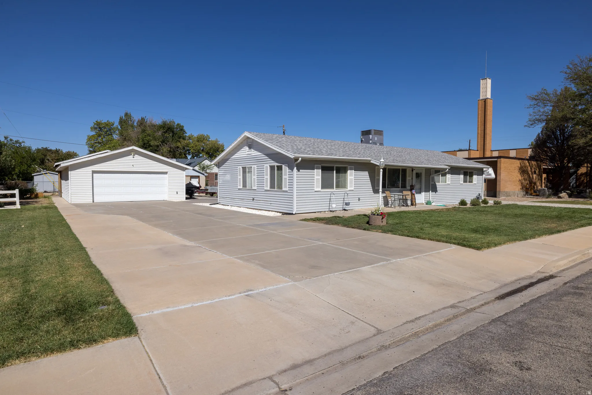 Single-story residence featuring siding, an attached garage, a detached garage, a concrete driveway, and a manicured lawn