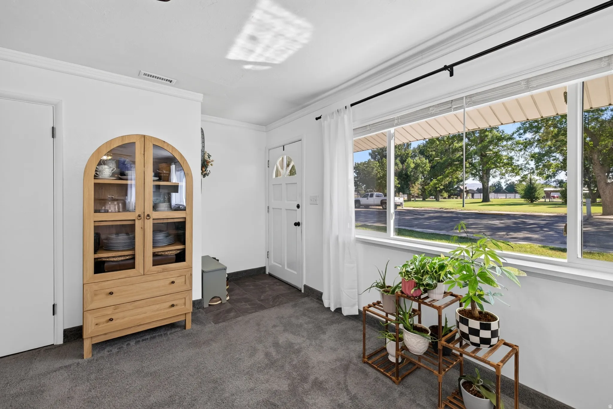 White interior door with a half-moon glass insert, large window with white trim, gray carpet flooring, white walls, and crown molding