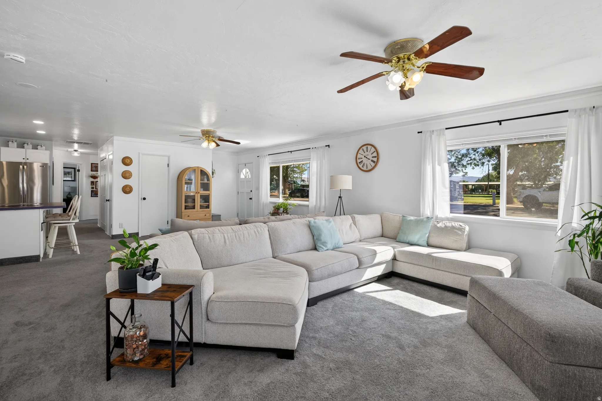 Spacious living area featuring light gray carpeting, multiple windows, and a ceiling fan