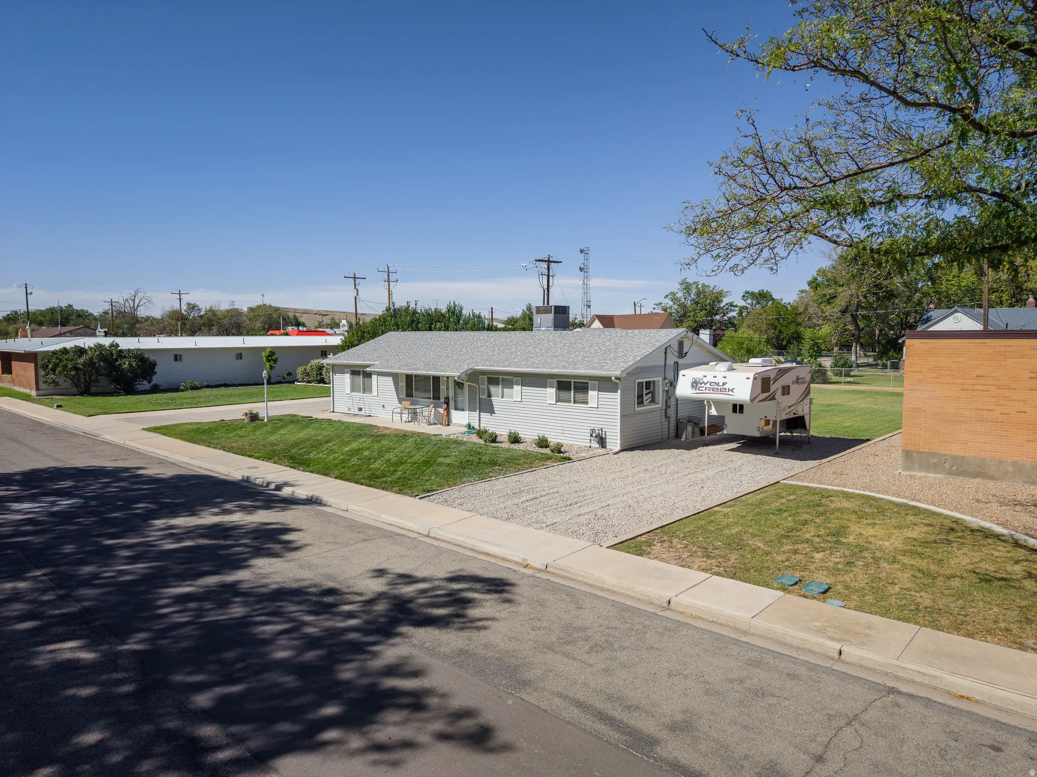 Light gray siding exterior with a gravel driveway and an expansive grassy area