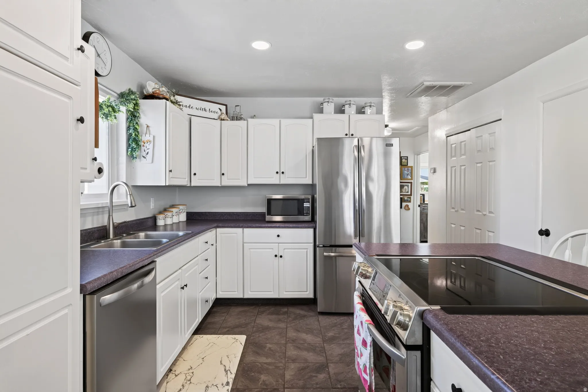 White cabinetry, stainless steel appliances, dual basin sink, integrated cooktop, and dark countertops