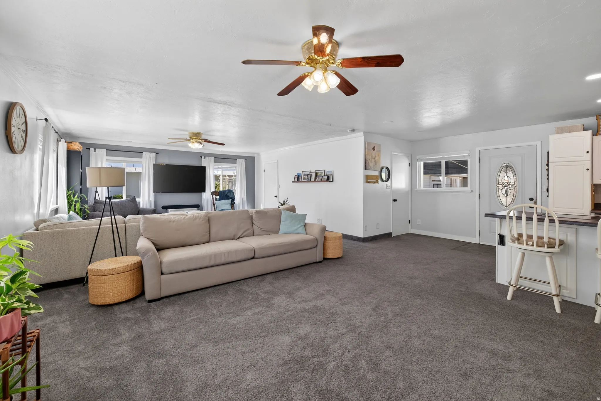 Open-concept living area with dark gray carpeting, multiple ceiling fans with integrated lighting, and white walls