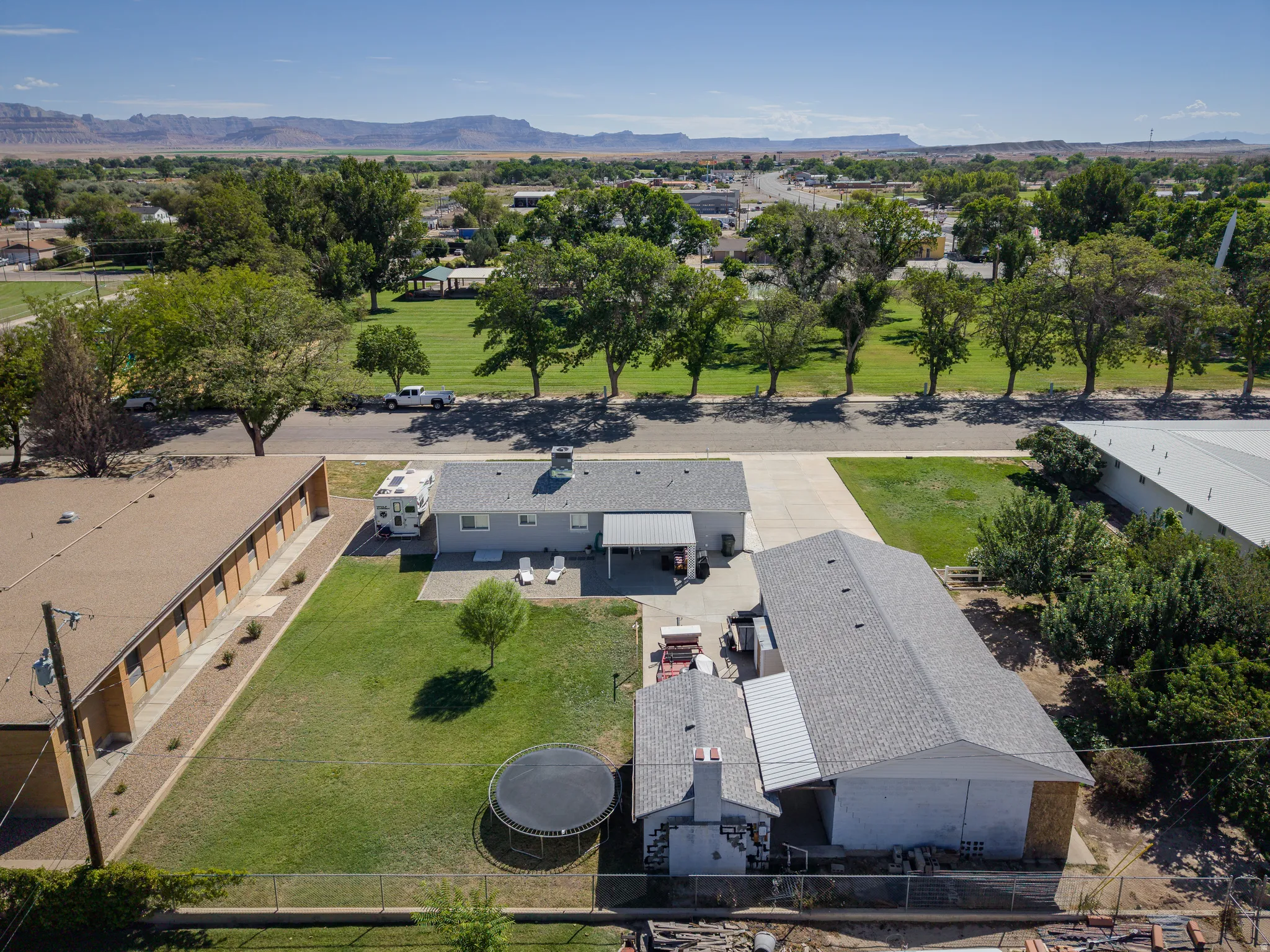 Expansive property featuring a main residence with an attached covered patio, a detached large auxiliary building with a shingle roof, a secondary detached structure with a pitched roof, and a substantial paved driveway