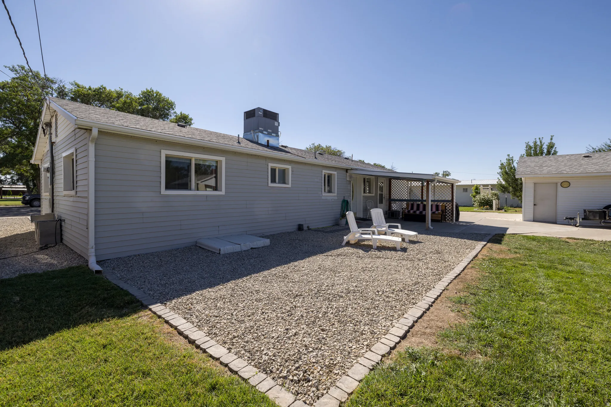 Ranch-style residence featuring light gray siding, white trim windows, and a covered back patio with latticework