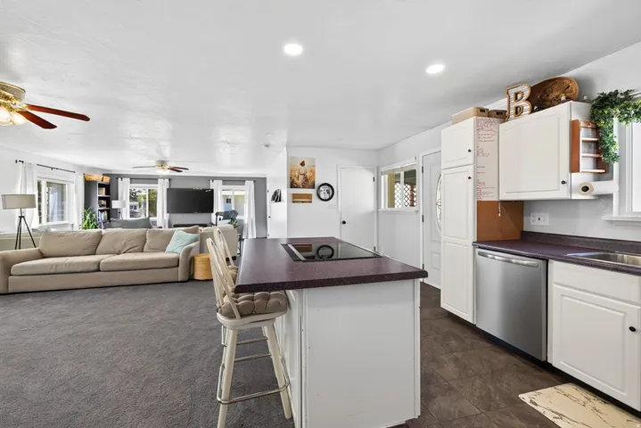 Kitchen island with cooktop and seating, white cabinetry, stainless steel dishwasher, and wood-finish flooring