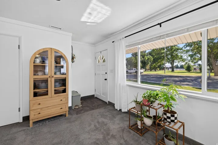 White interior door with a half-moon glass insert, large window with white trim, gray carpet flooring, white walls, and crown molding