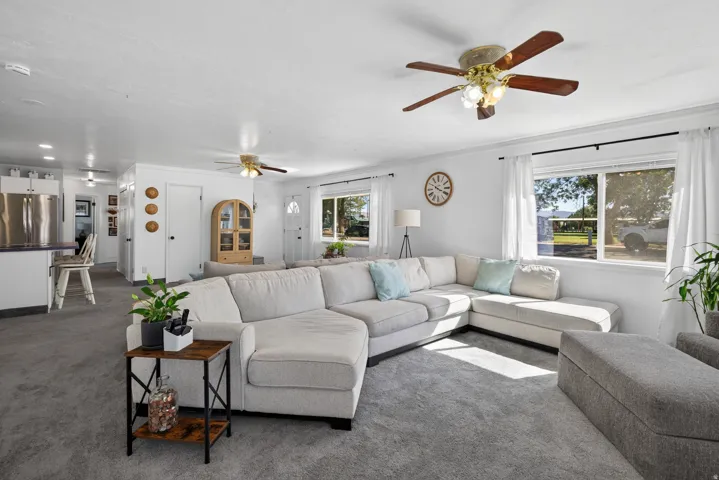 Spacious living area featuring light gray carpeting, multiple windows, and a ceiling fan