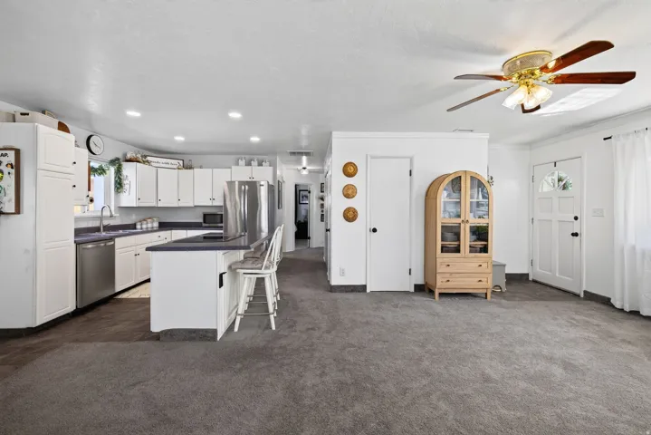 Integrated kitchen and living area featuring a kitchen island with seating, white shaker-style cabinetry, recessed lighting, and a ceiling fan