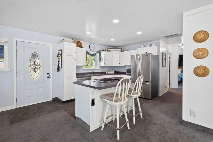 Kitchen featuring white cabinetry, an island with countertop seating, stainless steel refrigerator, and recessed lighting