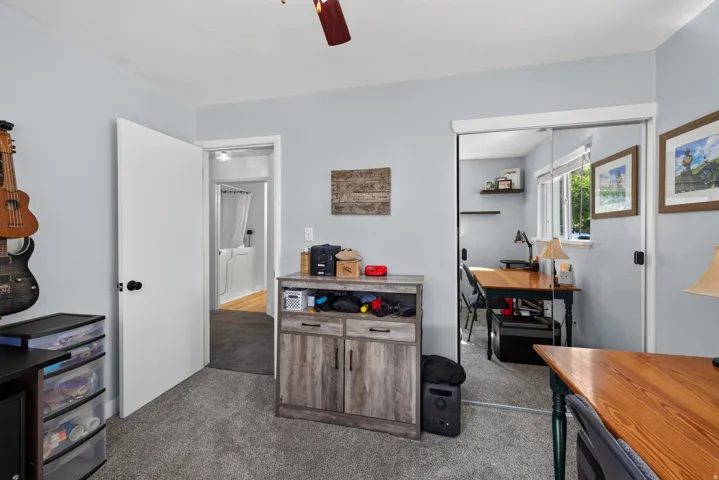 Carpeted room featuring a ceiling fan, a mirrored closet door, and a built-in wood-finish cabinet
