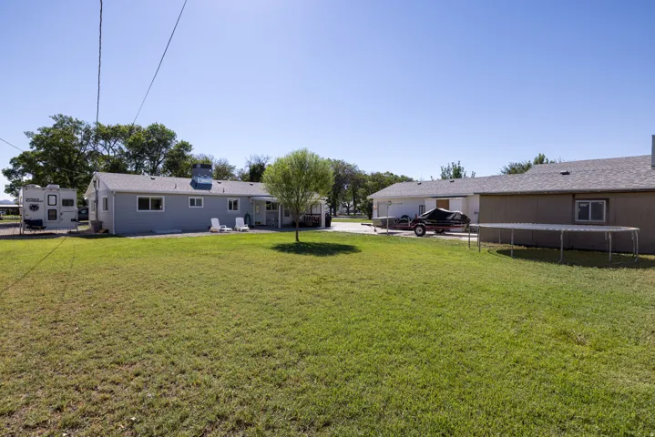Expansive grassy yard with mature trees, a light blue exterior residence, and an additional detached structure