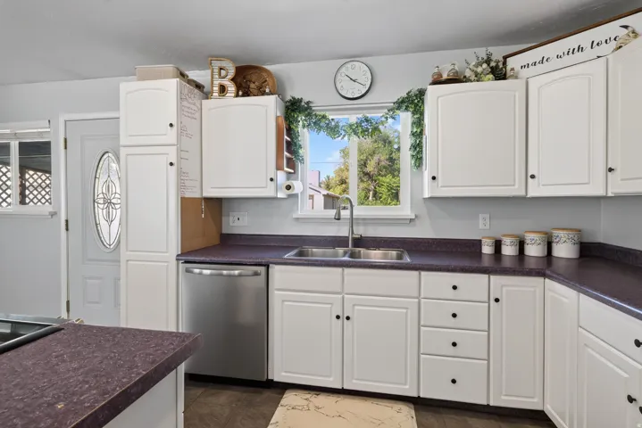 Kitchen featuring white cabinetry, a stainless steel dishwasher, a double basin sink with a high-arc faucet, and dark countertops