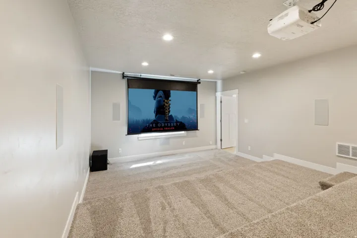 Dedicated media room featuring tiered carpeted flooring, recessed ceiling lighting, a mounted projector, and a retractable projection screen