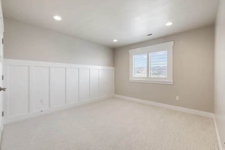 Recessed lighting, light-toned carpeting, board and batten wainscoting, window with white plantation shutters, and painted walls