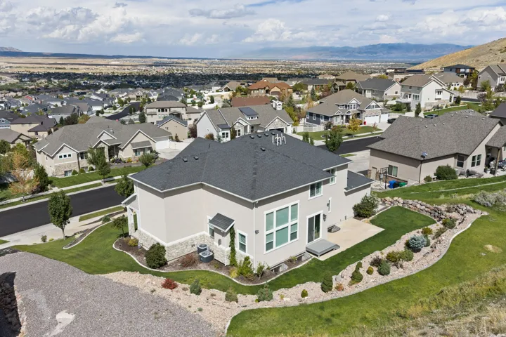 Expansive landscaped yard with a concrete patio, mature shrubs, and rock detailing